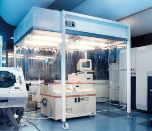 Operators in a Grade B background environment wearing full sterile gowning, including hoods, masks, and double gloves, preparing materials for the Grade A aseptic core.